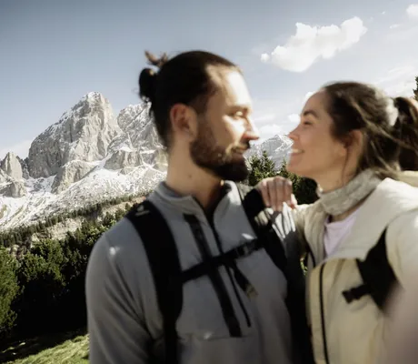 Paar mit Wanderkleidung vor schneebedeckten Bergen und blauem Himmel in den Dolomiten in der Nähe des PURMONTES Private Luxury Chalet