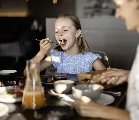 Mädchen mit Zöpfen ist genüsslich ein Stück Kuchen im DAS GERSTL Family Resort