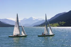 zwei Segelboote auf dem Reschensee mit Blick auf die verschneiten Berge