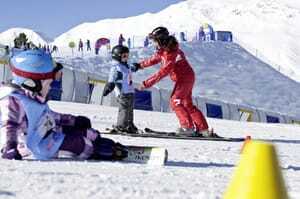 Skilehrerin in rotem Anzug gibt Kind Anweisungen auf der Piste
