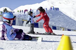 Skilehrerin in rotem Anzug gibt Kind Anweisungen auf der Piste