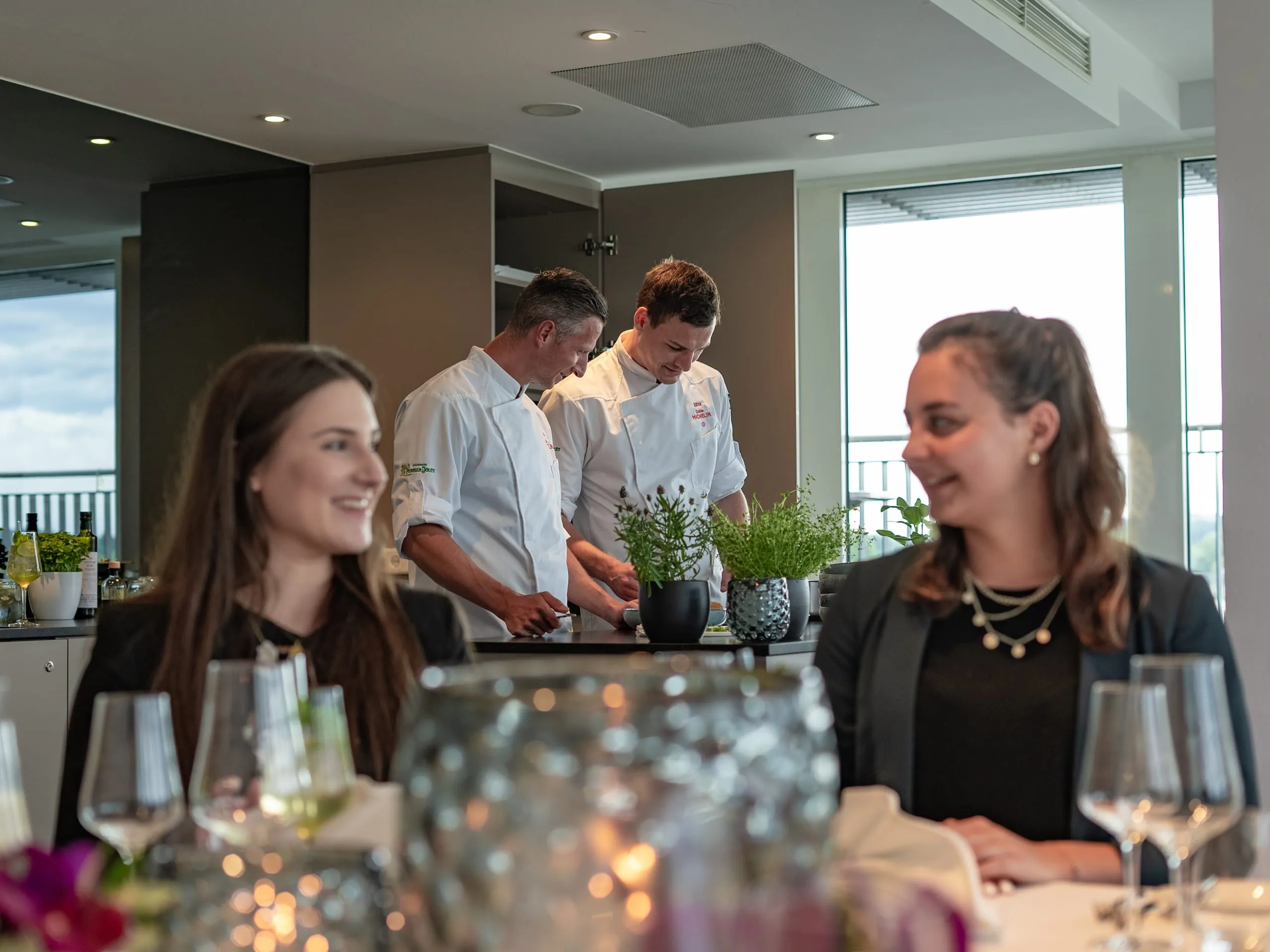 Zwei K&ouml;che im Hintergrund beim Live Cooking, im Vordergrund zwei Frauen die sich anlachen