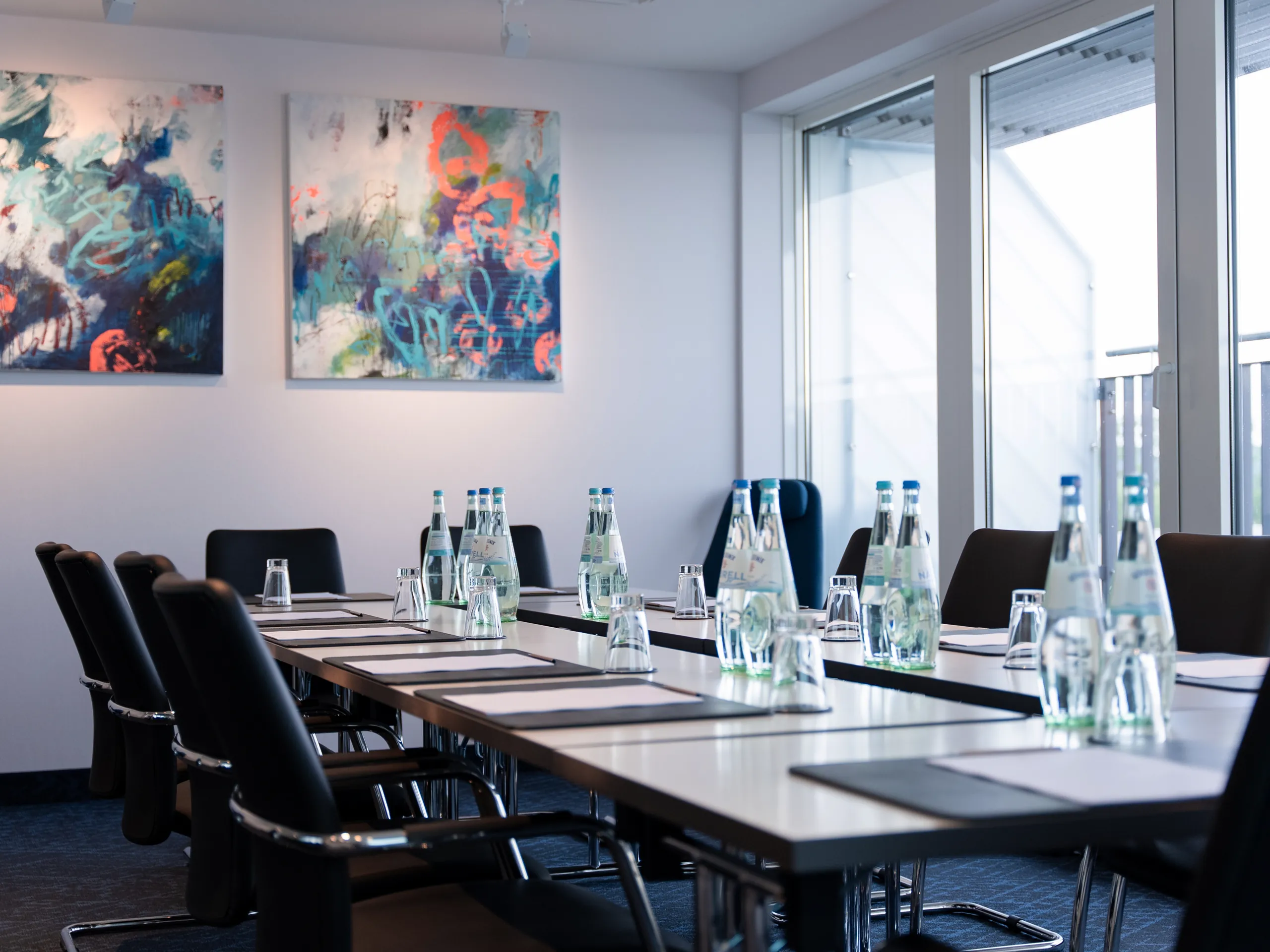 Tagungsraum mit gro&szlig;em Tisch und St&uuml;hlen und Bildern an der Wand