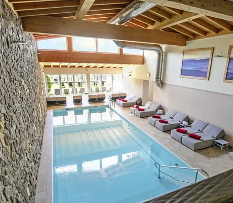 Indoorpool im Wellnesshotel Hofbräuhaus mit Steinwand, Liegen und großen Fenstern unter Holzbalkendecke