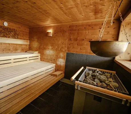 Holzsauna mit mehrstufigen Sitzbänken, Saunaofen mit Steinen und hängendem Wasserkessel im Wellnesshotel Hofbräuhaus