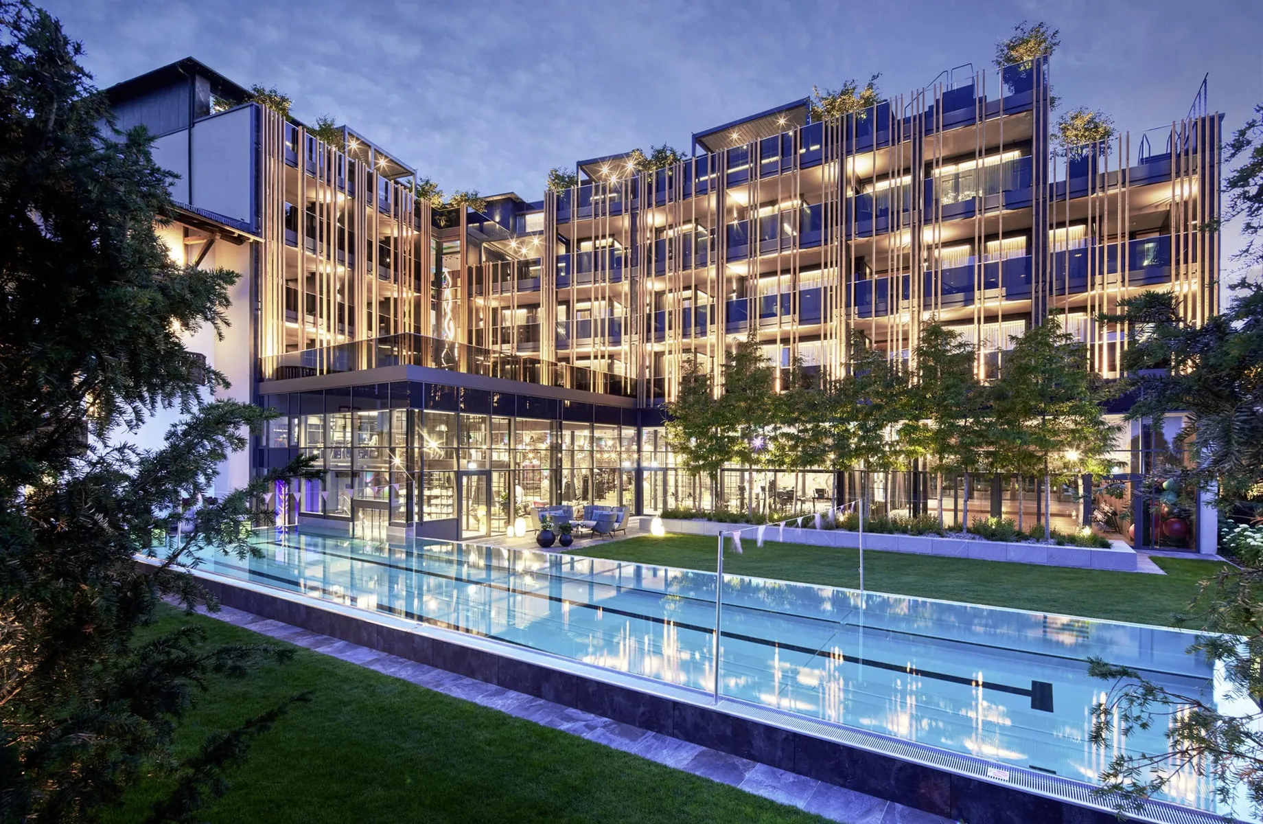 Außen-Schwimmbecken vor der beleuchteten Fassade des Wellnesshotel Jagdhof in der Abenddämmerung