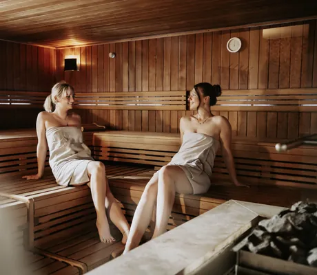 Zwei Frauen sitzen in einer Sauna des Wellnesshotels Randsbergerhof, jeweils in ein Handtuch gewickelt