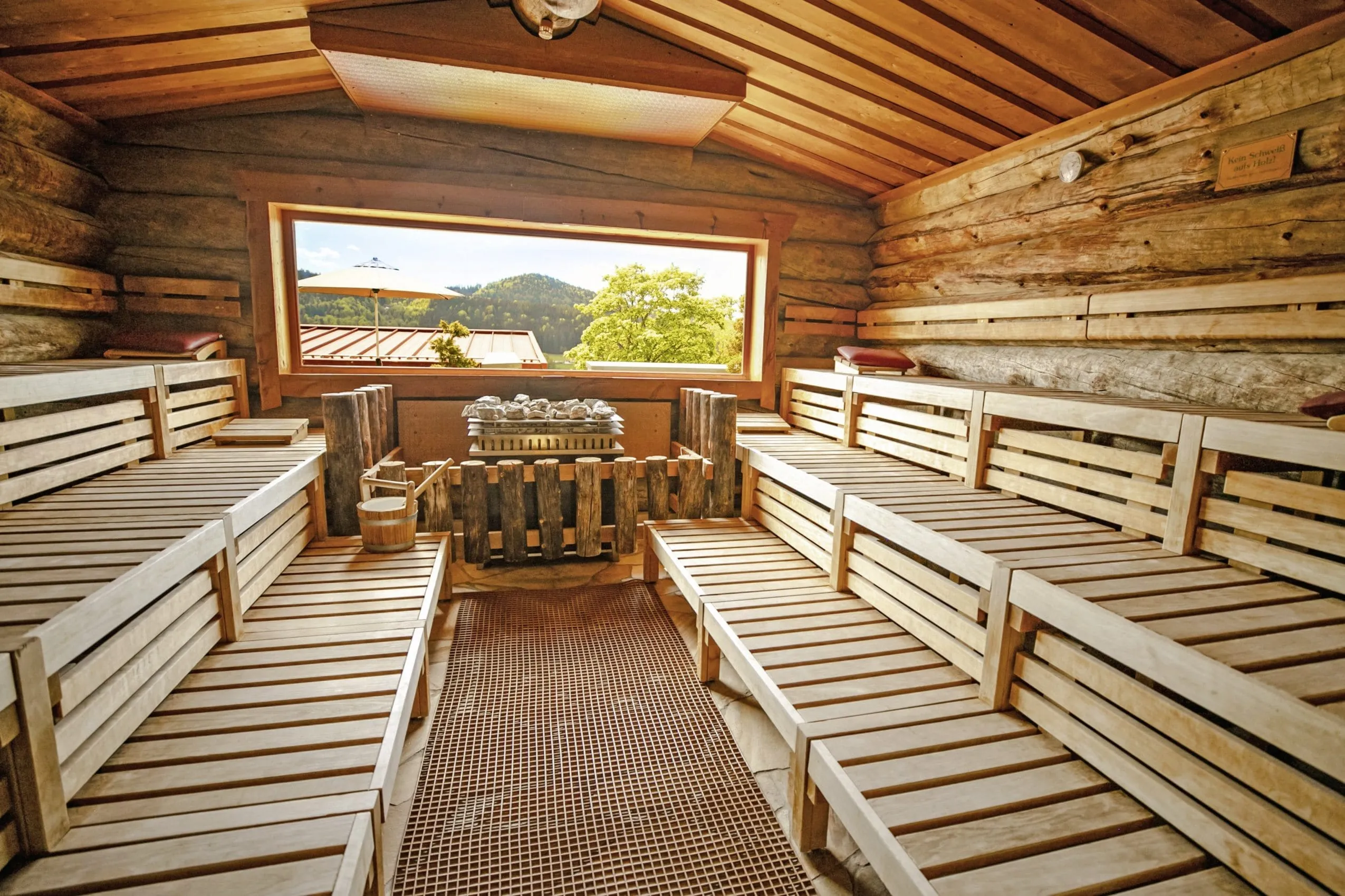 Kelosauna des Wellnesshotel Hofbr&auml;uhaus mit hellen Holzliegen, Natursteinboden und gro&szlig;em Fenster mit Blick in die Natur