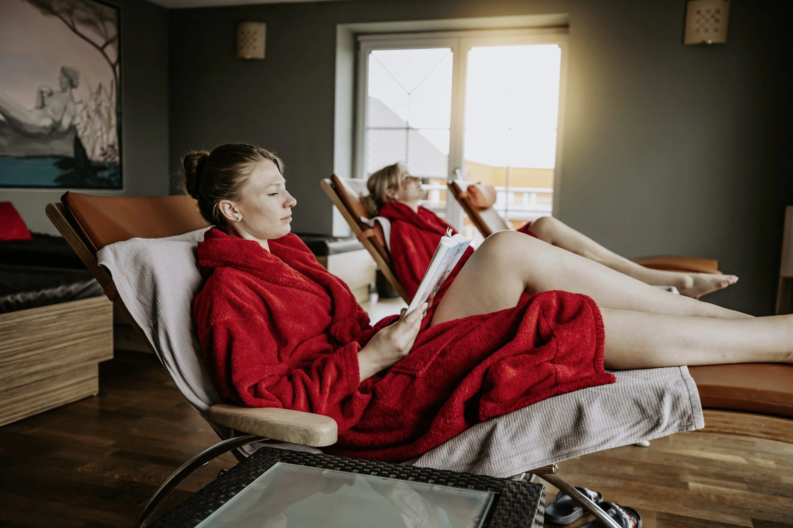Frauen in roten Badem&auml;nteln entspannen auf Wellnessliegen im Ruheraum des Wellnesshotel Randsbergerhof