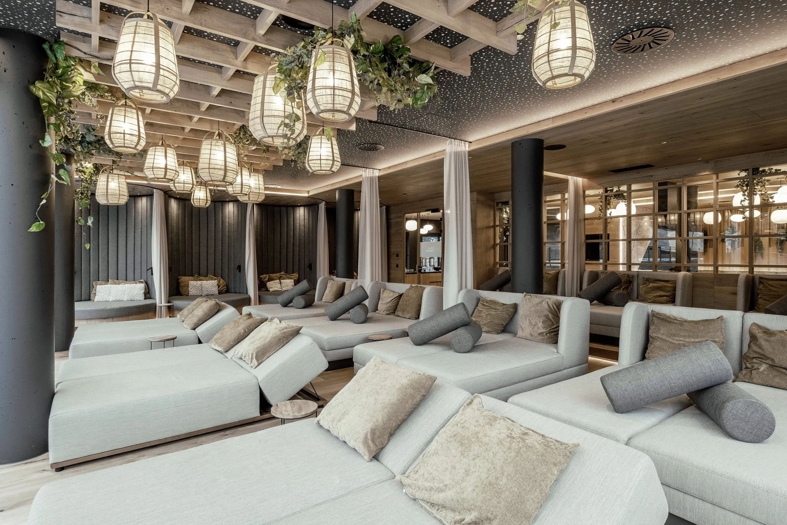 Hellgraue Ruheliegen mit Kissen im Wellnessbereich des Wellness & Naturhotel Tonihof****S, Holzgitter mit H&auml;ngelampen und Pflanzen an der Decke