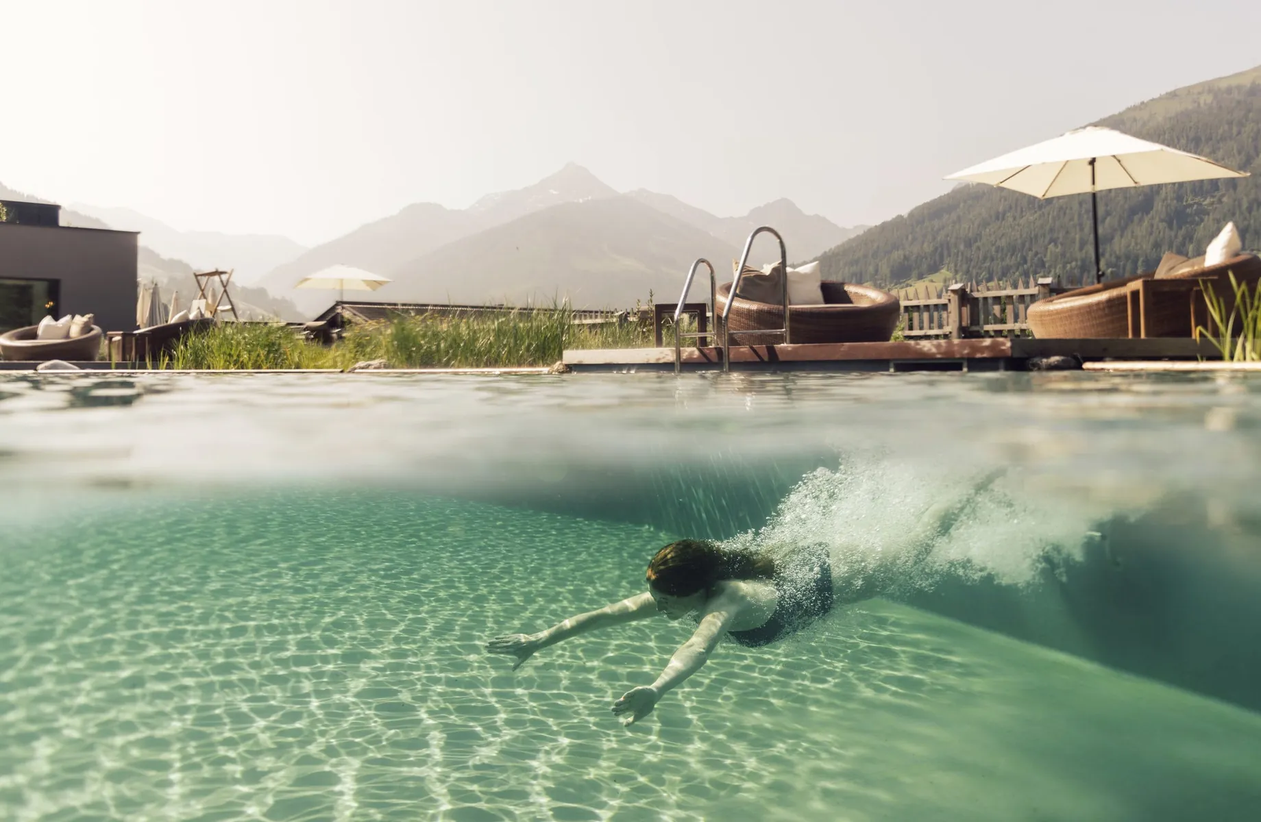Frau taucht in den Outdoorpool des Der Böglerhof – pure nature spa resort ein