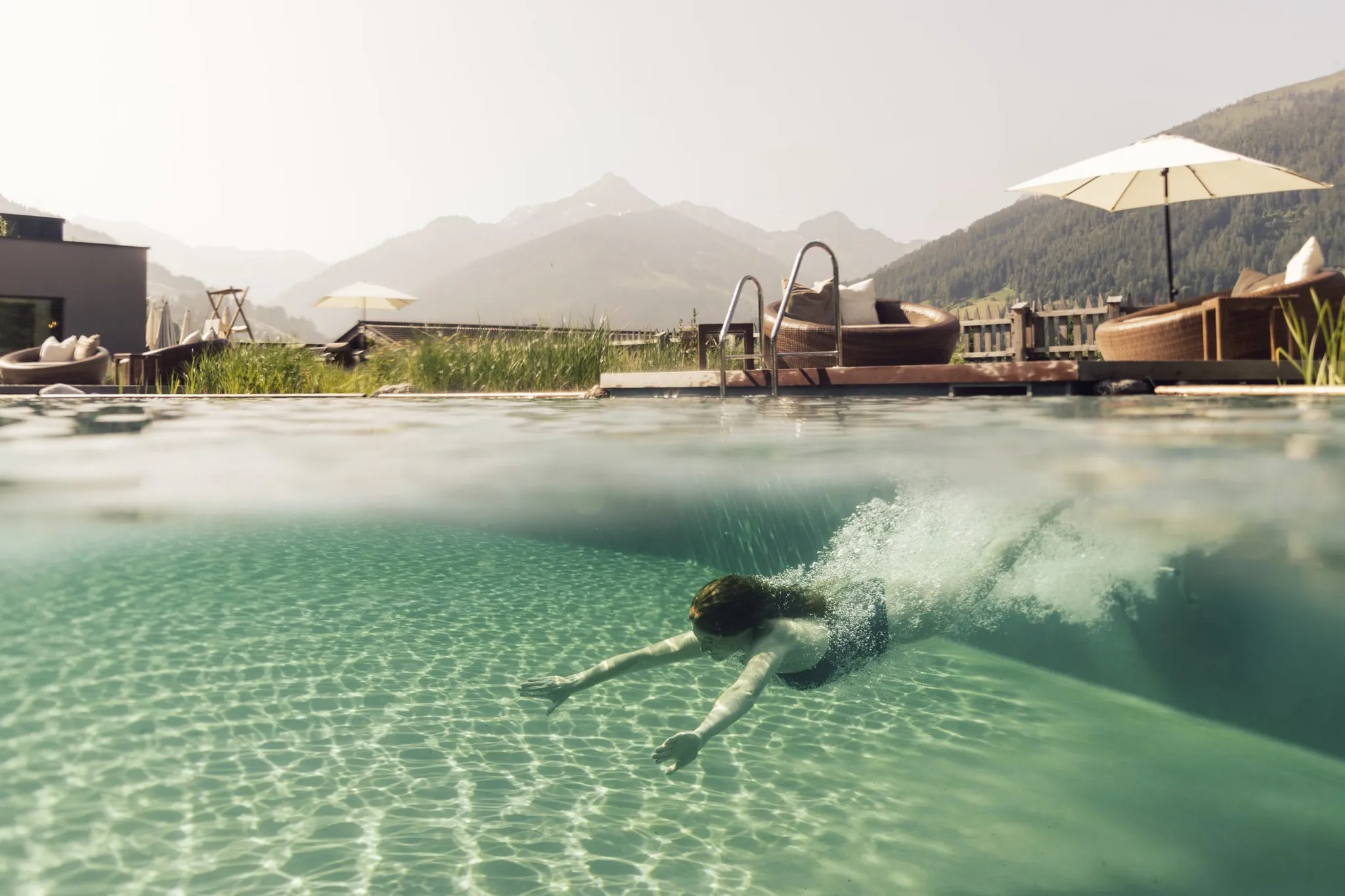 Frau taucht in den Outdoorpool des Der Böglerhof – pure nature spa resort ein
