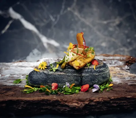 Gourmetgericht des Trofana Royal Resort mit Blüten und Kräutern auf schwarzem Stein und Holzplatte angerichtet