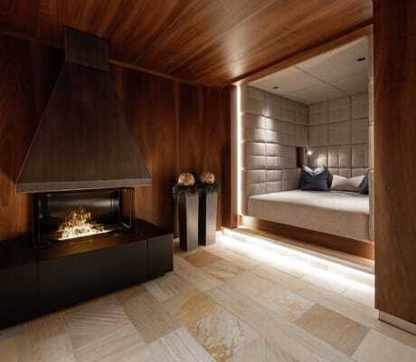 Gemütlicher Spabereich mit modernem Kamin, eingebauter Sitznische mit Kissen und Holzwänden im Trofana Royal Resort