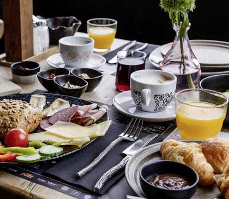 Gedeckter Frühstückstisch im mama thresl mit Vollkornbrötchen, Aufschnitt, Käse, Gurken, Tomate und Paprika, dazu Croissants, Kaffee und Orangensaft