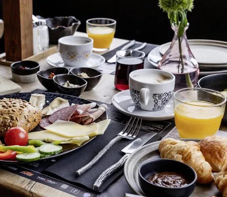 Gedeckter Frühstückstisch im mama thresl mit Vollkornbrötchen, Aufschnitt, Käse, Gurken, Tomate und Paprika, dazu Croissants, Kaffee und Orangensaft