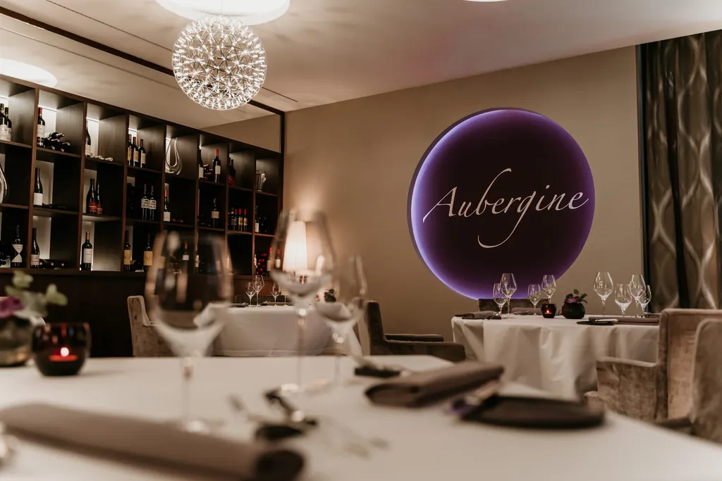 Restaurant Aubergine: Weingl&auml;ser auf Tischen mit wei&szlig;en Tischt&uuml;chern, im Hintergrund ein Weinregal