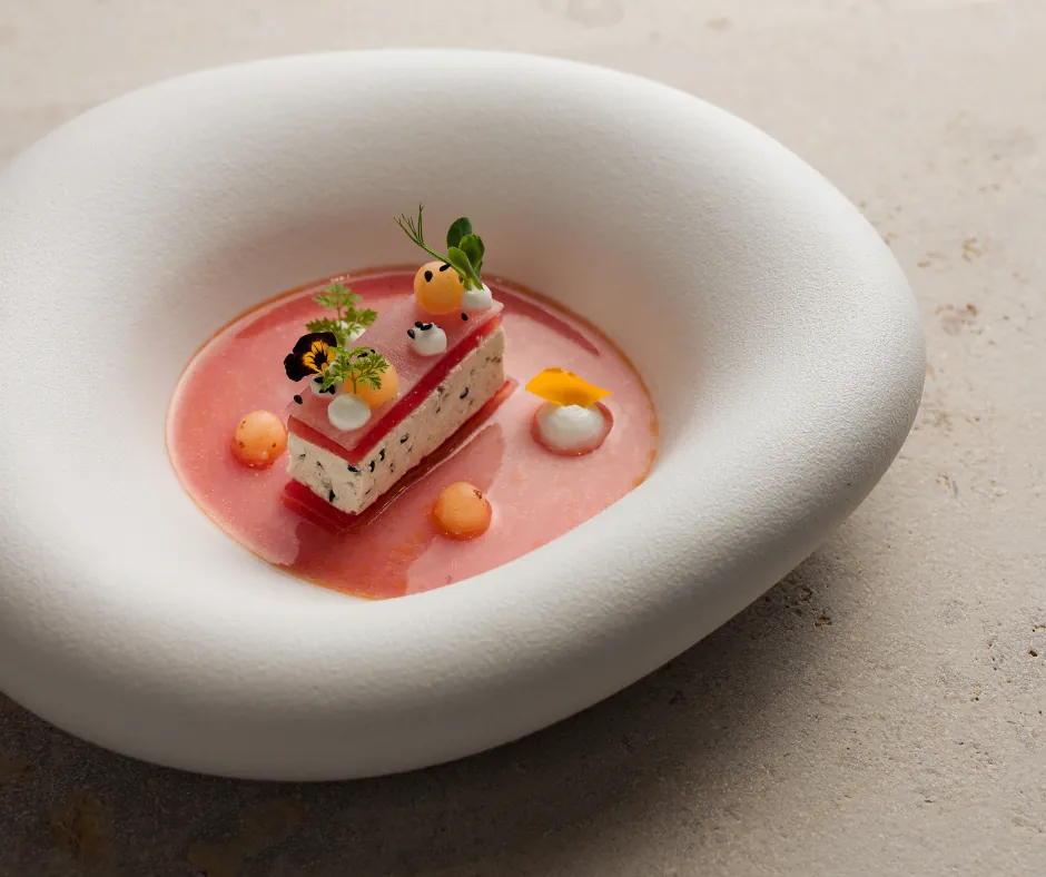 Restaurant Aubergine: Tofu mit Melone fein angerichtet auf einem runden tiefen Keramikteller der auf einer Steintischplatte steht