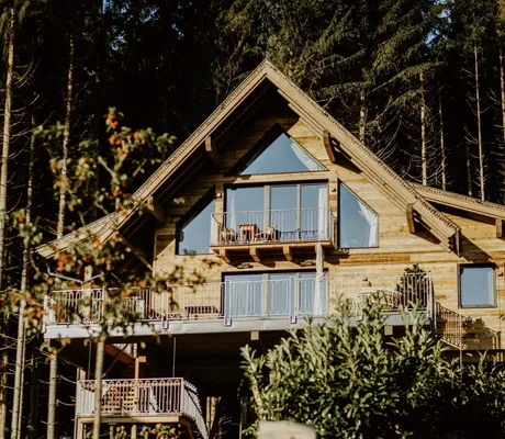 Baumhaus des Wander- und Wellnesshotel Gassner mit spitzem Dach und großen Fenstern, umgeben von Bäumen und Gartenpflanzen. Balkone mit Geländern sind sichtbar