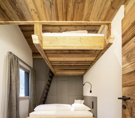 Kinderzimmer im Baumhaus des Wander- und Wellnesshotel Gassner mit einem Doppelbett aus Holz, einem Hochbett mit schwarzer Leiter, Holzdecke, Fenster und einem kleinen, schwarzen Beistelltisch