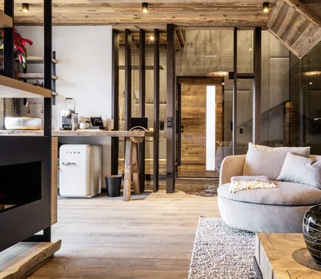 Wohnbereich des Baumhauses des Wander- und Wellnesshotel Gassner mit Holzverkleidung, Sessel, Sofa, Sofatisch und Blick auf die Küchenzeile mit Mini-Kühlschrank