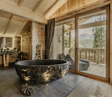 Schwarze freistehende Badewanne mit Marmoroptik im Chalet des Chalet Resort ZU KIRCHWIES mit großen Fenstern und Blick auf eine Terrasse und Berge