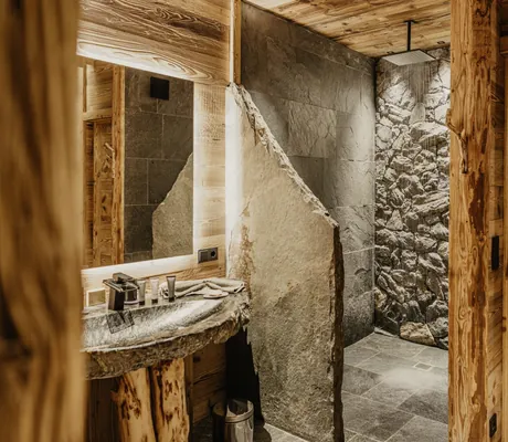 Badezimmer mit Naturstein-Dusche, Holzverkleidung, Steinwaschbecken und großem Spiegel im Chalet Resort ZU KIRCHWIES