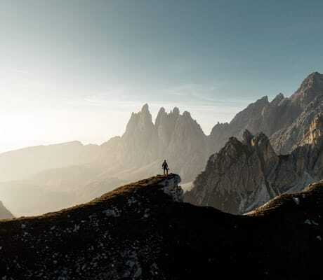 Person steht auf Felsvorsprung mit Blick auf Bergpanorama der Dolomiten bei Sonnenaufgang in der Nähe des Chalet Resort ZU KIRCHWIES