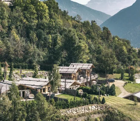 Mehrere Chalets des Chalet Resort ZU KIRCHWIES mit Schindeldächern in einem bewaldeten Bergtal mit Bergen im Hintergrund
