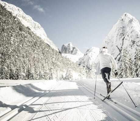 Langläufer in Sportkleidung von hinten auf präparierter Loipe vor schneebedeckten Bergen und Tannen in der Nähe des Chalet Resort ZU KIRCHWIES