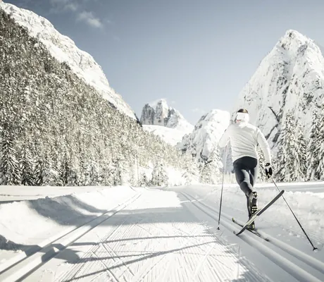 Langläufer in Sportkleidung von hinten auf präparierter Loipe vor schneebedeckten Bergen und Tannen in der Nähe des Chalet Resort ZU KIRCHWIES