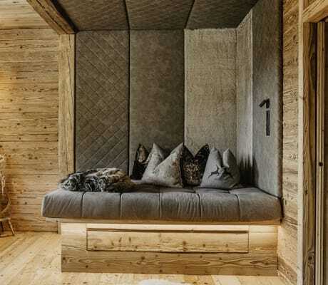 Gemütliche Sitzecke mit grauem Polster, mehreren Kissen und Holzverkleidung im Chalet Resort ZU KIRCHWIES