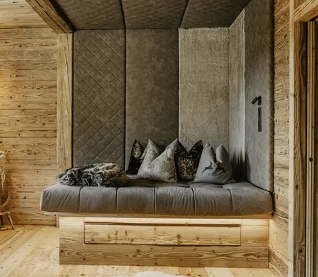 Gemütliche Sitzecke mit grauem Polster, mehreren Kissen und Holzverkleidung im Chalet Resort ZU KIRCHWIES
