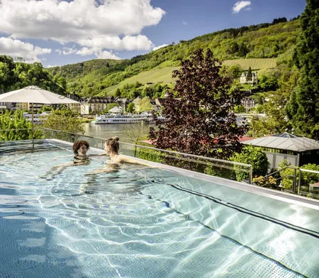zwei Frauen unterhalten sich im Outdoorpool des Moselschlösschen Spa & Resort mit Blick auf die Mosel