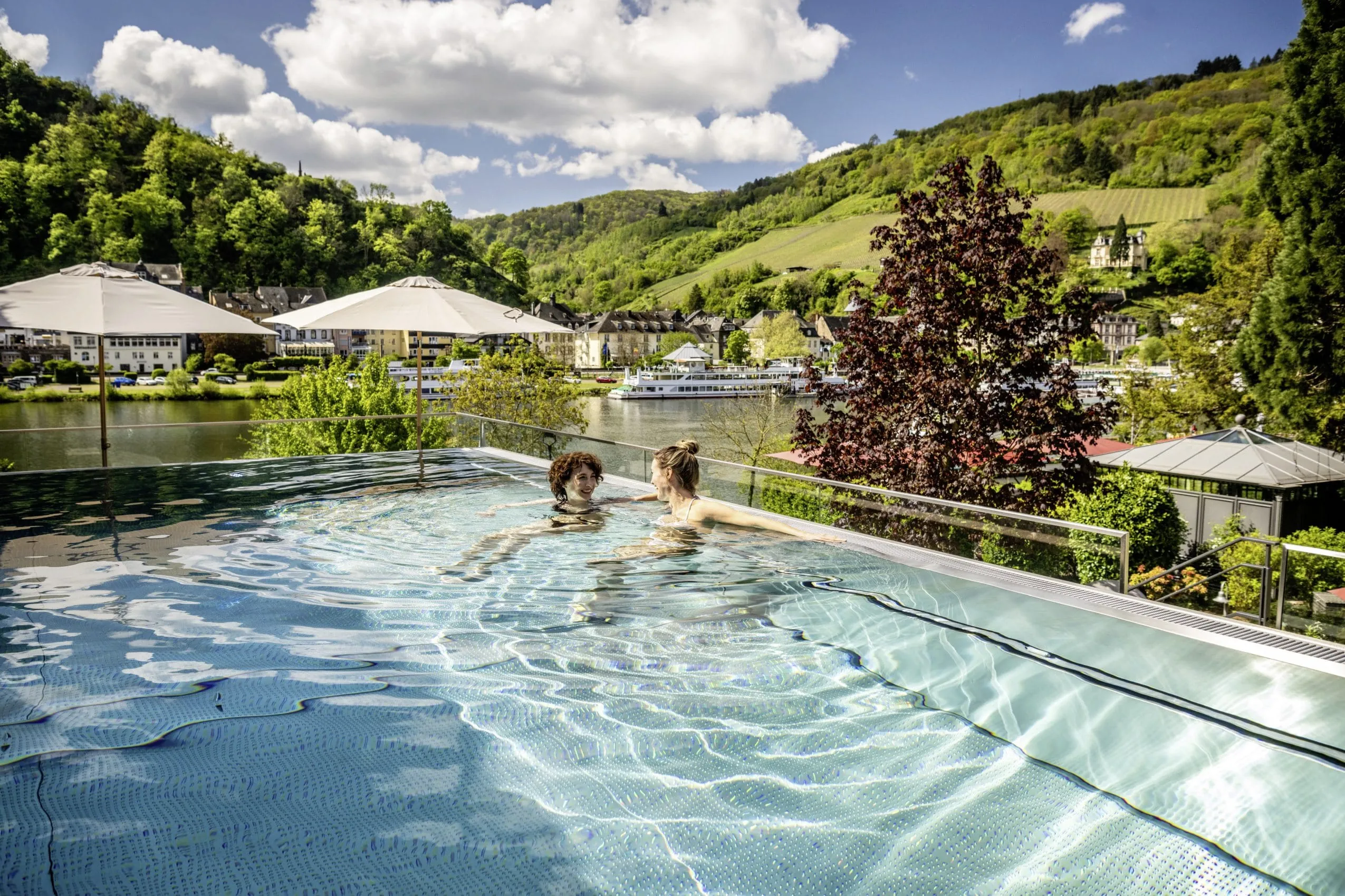 zwei Frauen unterhalten sich im Outdoorpool des Moselschl&ouml;sschen Spa & Resort mit Blick auf die Mosel