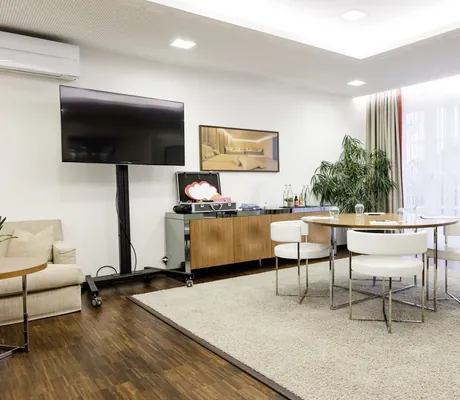 Konferenzraum mit rundem Holztisch, sechs weißen Stühlen, großem Fernseher, Flipchart und Pflanze im Wald & Schlosshotel Friedrichsruhe