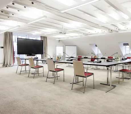 Heller Tagungsraum im Wald & Schlosshotel Friedrichsruhe mit U-förmiger Tischanordnung, Stühlen mit roten Sitzflächen, großem Bildschirm und Flipchart