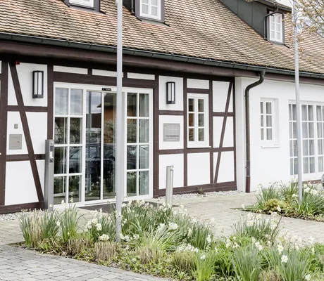 Außenansicht der Tagungsremise im Wald& Schlosshotel Friedrichsruhe mit Fachwerkfassade, Uhrenturm und Frühjahrsblumen