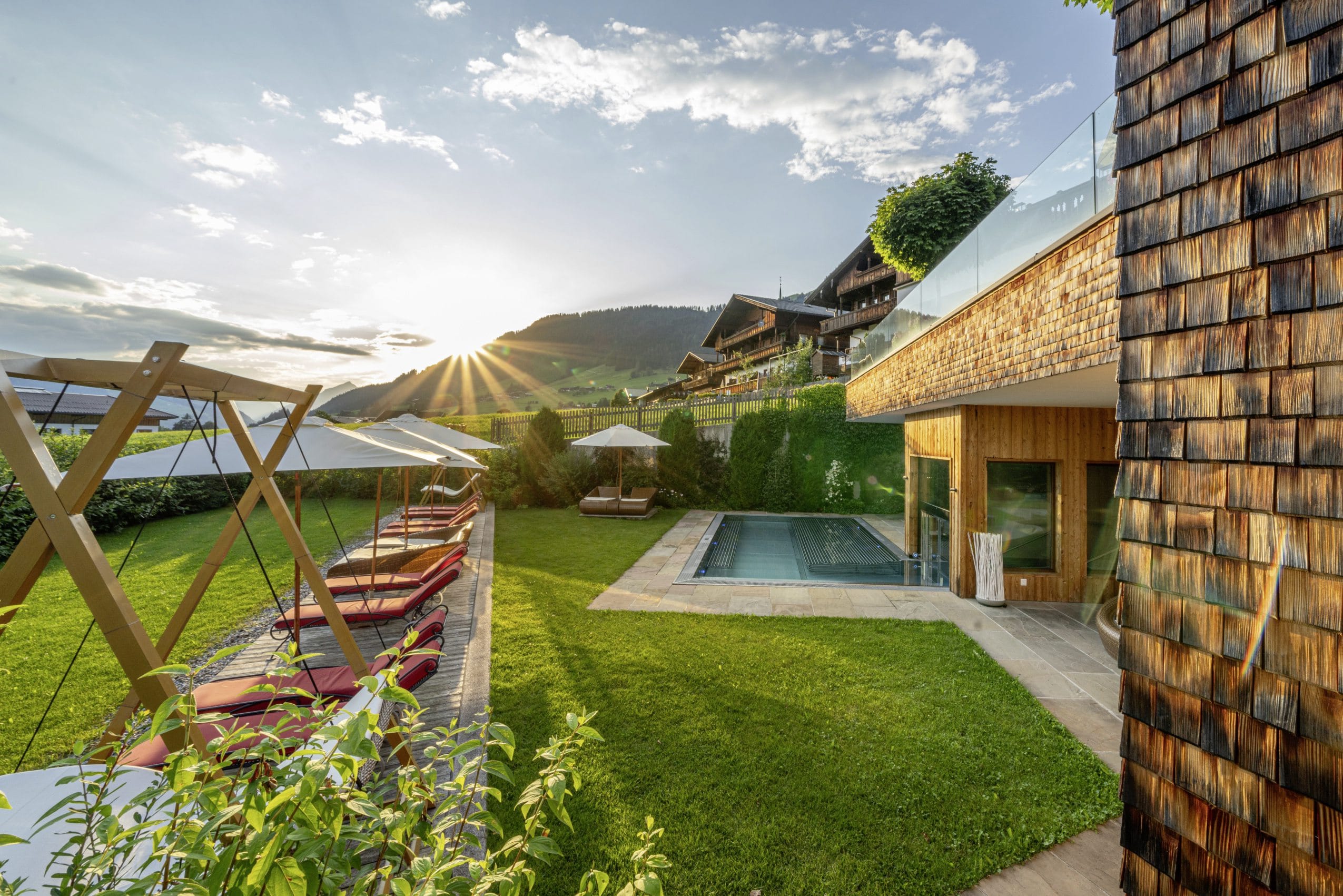 Outdoorpool und Hängeliegen vor verschindelter Fassade des Alpbacherhof in der Abendsonne