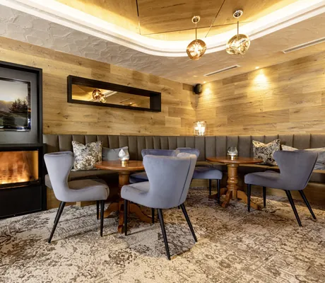 Loungeecke mit grauen Polstersesseln vor holzvertäfelter Wand und mit LED-Kamin im Alpbacherhof