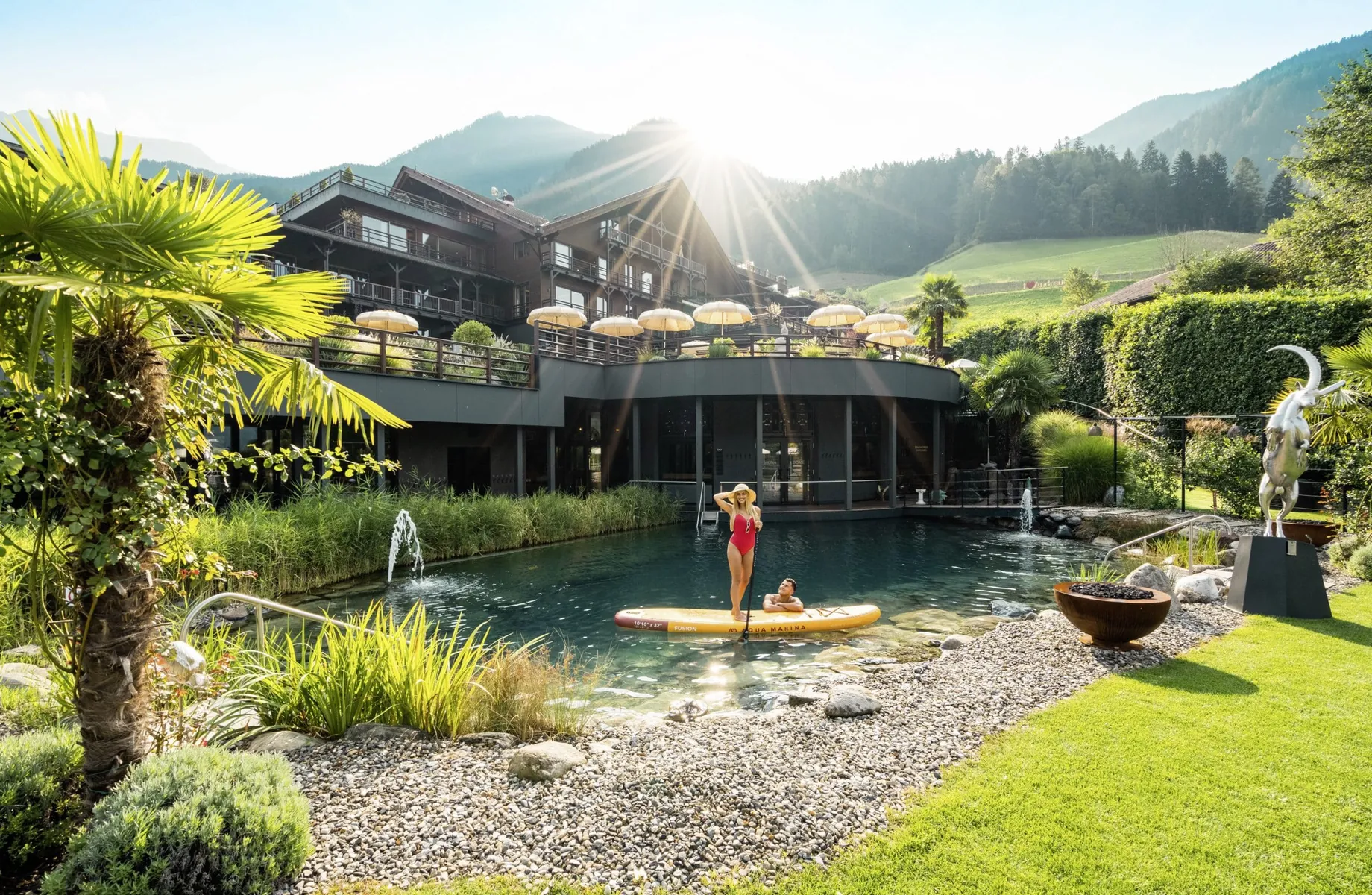 Frau in rotem Badeanzug auf einem gelben SUP auf dem Teich vor der Fassade des Andreus Resort