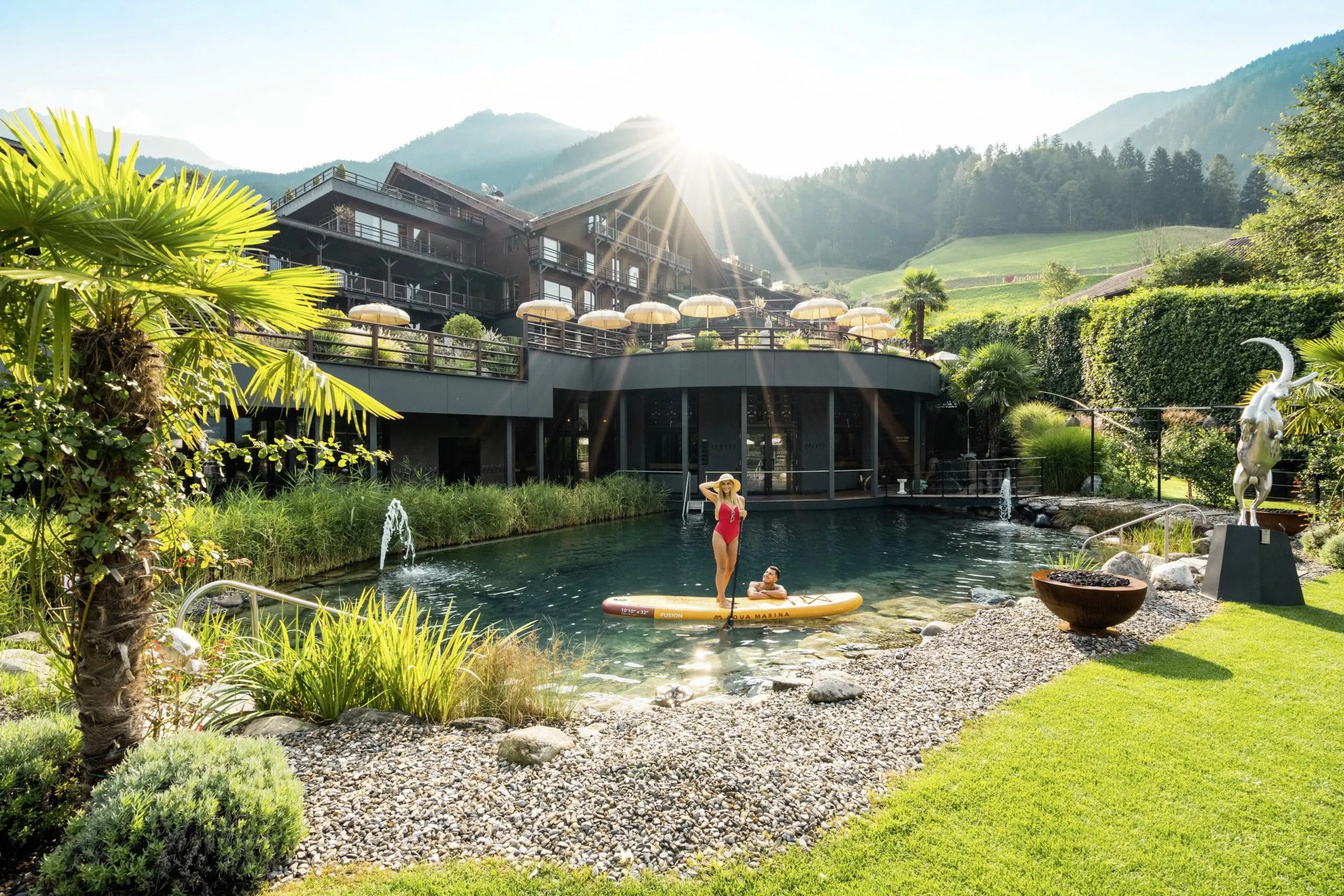 Frau in rotem Badeanzug auf einem gelben SUP auf dem Teich vor der Fassade des Andreus Resort