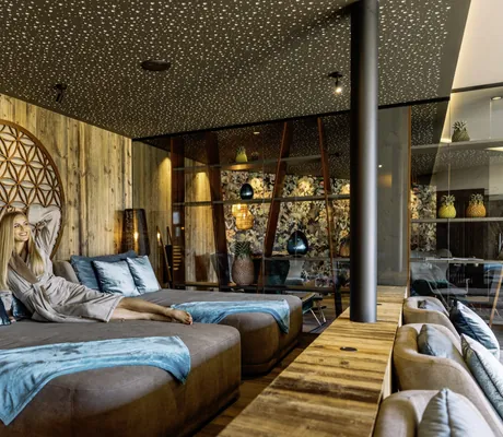 blonde Frau in grauem Bademantek auf grauem Ruhebett mit türkisen Kissen im Andreus Resort