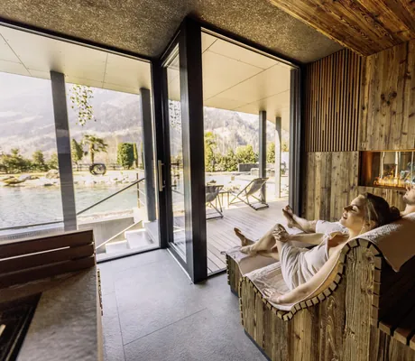Paar eingehüllt in Handtüchern liegt auf Saunaliegen in der Sauna und schaut auf Teich des Andreus Resort