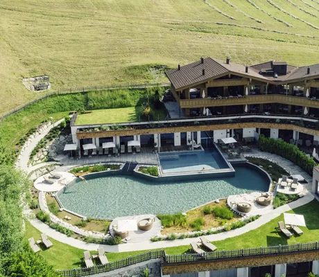 Außenansicht des Der Böglerhof – pure nature spa resort mit großem, ovalen Natursee und mehreren Liegen auf der Terrasse