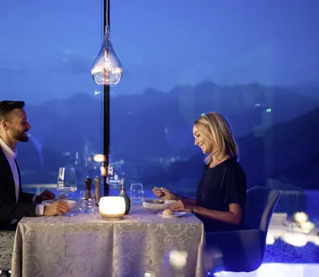 Paar in Abendgarderobe sitzt am Panoramafenster im Restaurant des Das Gerstl Alpine Retreat