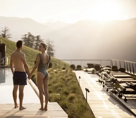 Paar in Badeoutfit steht Hand in Hand am Beckenrand des Outdoorpool des Das Gerstl Alpine Retreat