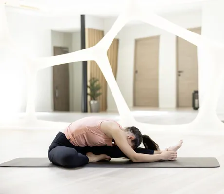 dunkelhaarige Frau mit Zopf macht Yoga im Yogaraum mit weißen Ornamenten auf dem Spiegel im Das Gerstl Alpine Retreat