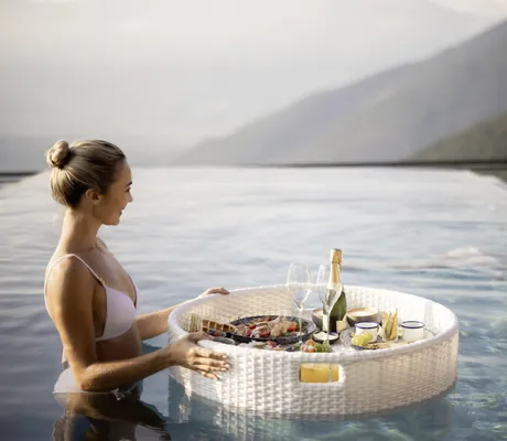 Frau in weißem Bikini schiebt ein schwimmendes weißes Tablett mit Frühstück über das Wasser des Pools im Das Gerstl Alpine Retreat