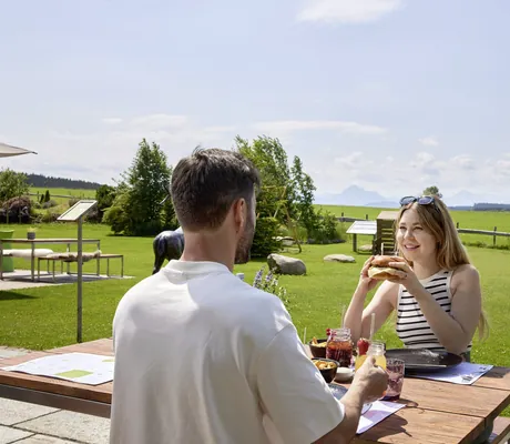 junges Paar frühstückt an einem Holztisch mit Blick über die Wiesen am Das Weitblick Allgäu